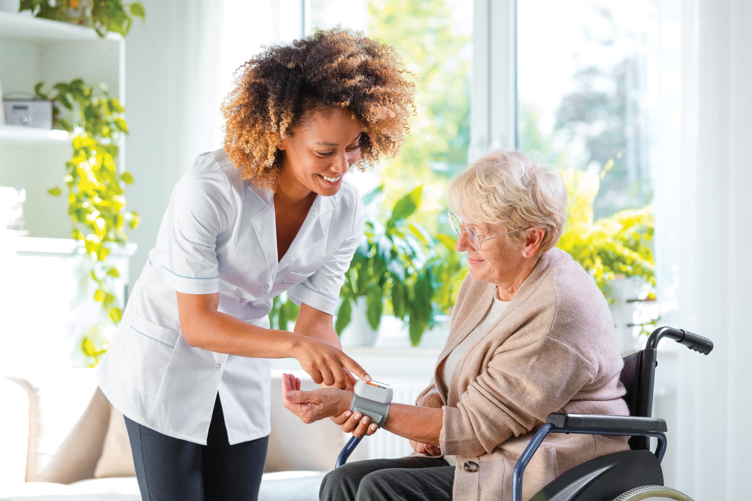 A smiling home nurse takes an older woman's blood pressure.