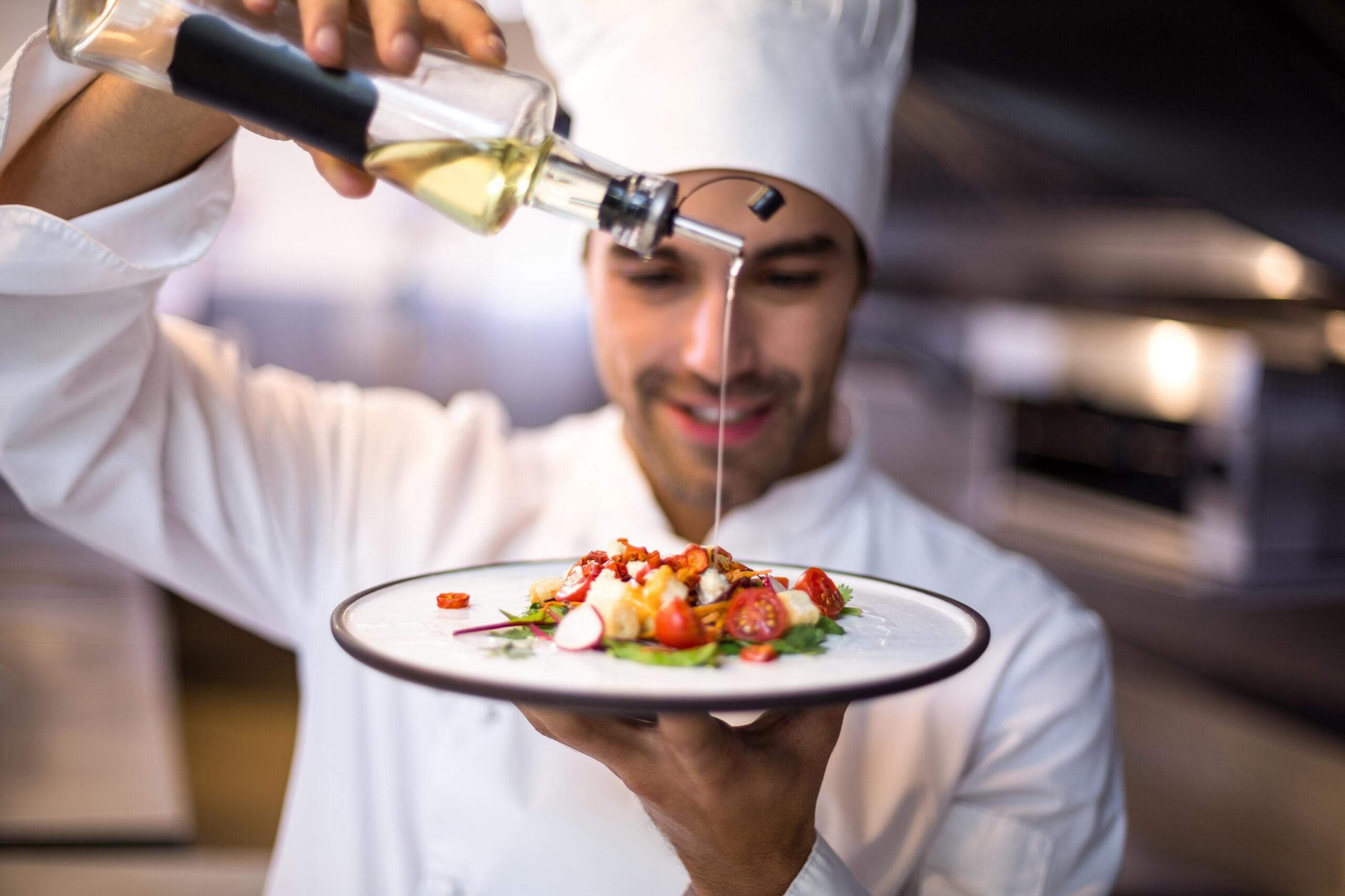 A chef concentrates on pouring oil to garnish a gourmet meal.