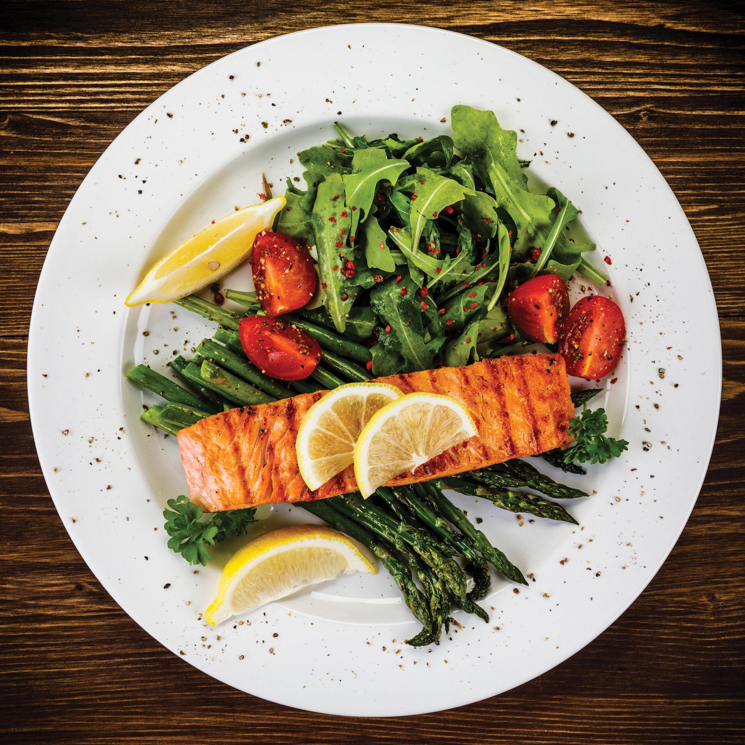 Gourmet grilled salmon with asparagus and arugula on wooden table.