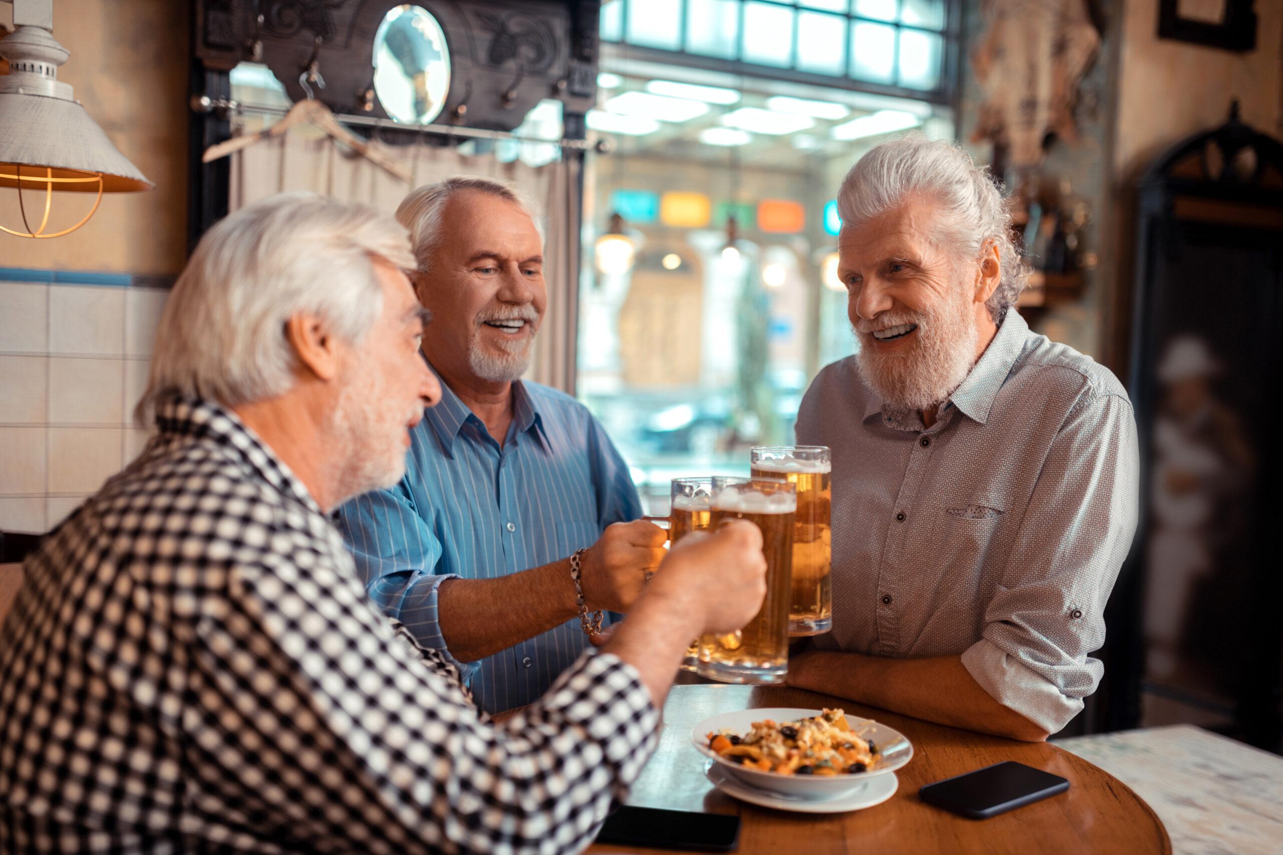 Three older men cheers beer glasses